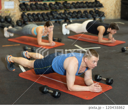 Middle-aged sportsman in activewear standing in plank exercise on mat as part of CrossFit bodybuilding group training in gym Middle-aged sportsman in activewear standing in plank exercise on mat as part of CrossFit bodybuilding group training in gym 120438862