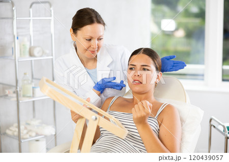 Girl client of cosmetologist frowns forehead to determine area of administration drug from wrinkles 120439057