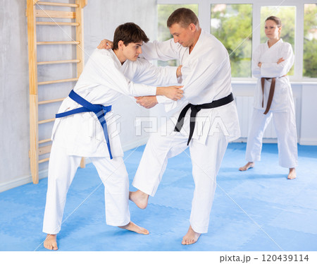Judo or jiu-jitsu classes - two men practicing grabbing and throwing on sports mats under the guidance of trainer 120439114