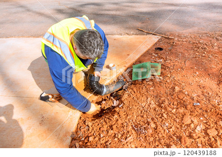 Worker wearing safety vest is crouched down, fixing drainage pipe in residential neighborhood at during construction site 120439188