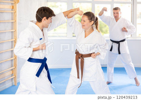 Woman and man in pairs exercising karate movements during group training in gym Woman and man in pairs exercising karate movements during group training in gym 120439213