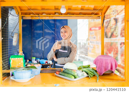 Smiling Vendor at a Colorful Food Stall Surrounded by Fresh Vegetables 120441510