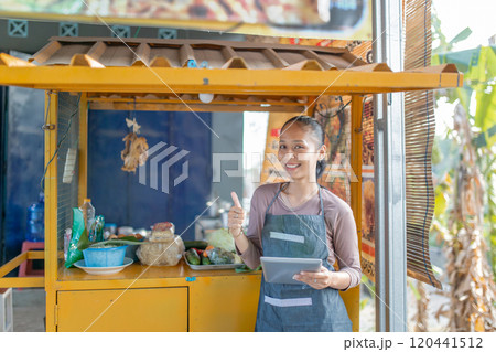 Cheerful Vendor at a Lively Food Cart Located in an Outdoor Setting Filled with People Cheerful Vendor at a Lively Food Cart Located in an Outdoor Setting Filled with People 120441512