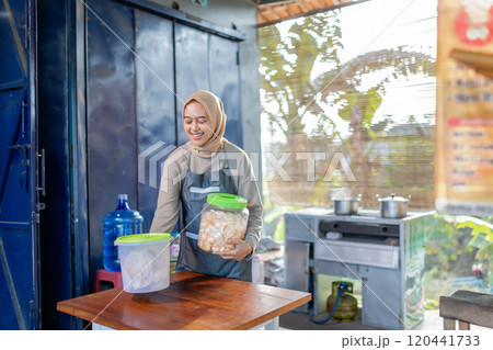 A cheerful young woman diligently serves fresh snacks at a small food stall 120441733