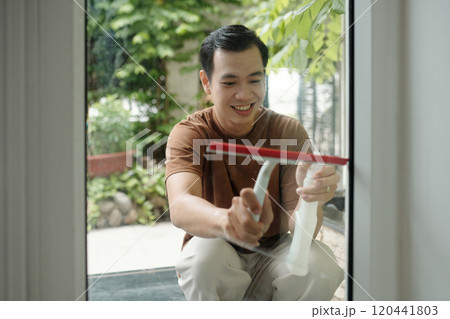 Smiling Young Man Cleaning Windows in Outdoor Setting Smiling Young Man Cleaning Windows in Outdoor Setting 120441803