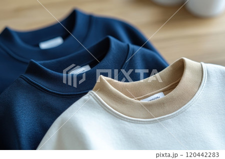 Close-up of three plain sweatshirts in shades of blue and beige showcasing minimalist fashion and soft fabric texture 120442283
