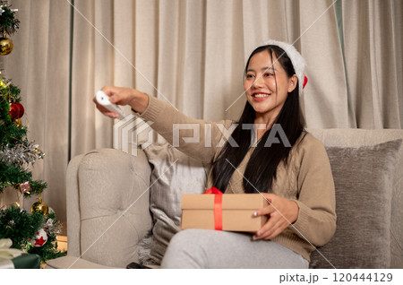 A cheerful woman celebrates the Christmas holiday alone at home, enjoying watching TV on the sofa. A cheerful woman celebrates the Christmas holiday alone at home, enjoying watching TV on the sofa. 120444129