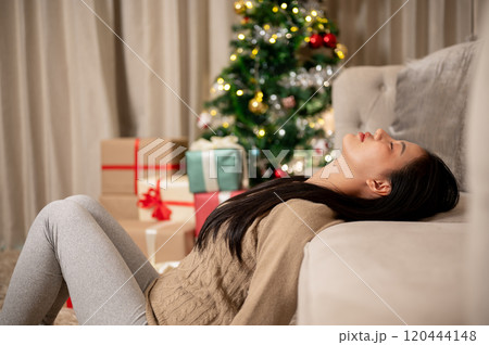 A carefree, calm Asian woman in cozy warm clothes takes a peaceful nap in the living room. 120444148