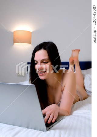 Portrait of smiling brunette woman is typing message on laptop lying in bed. Portrait of smiling brunette woman is typing message on laptop lying in bed. 120445087