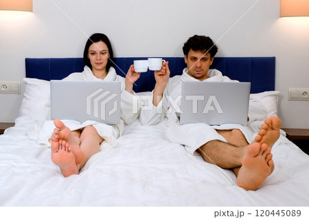Man and woman freelancers drinking morning coffee and working on laptops in bed. Man and woman freelancers drinking morning coffee and working on laptops in bed. 120445089