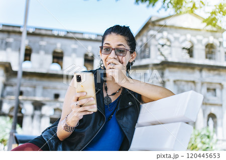 An attractive girl sitting on the cell phone smiling, Girl sitting on a bench texting on her cell phone, Urban style girl sitting on a bench with her cell phone An attractive girl sitting on the cell phone smiling, Girl sitting on a bench texting on her cell phone, Urban style girl sitting on a bench with her cell phone 120445653