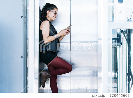 A person texting in the elevator, Attractive girl using her cell phone at the elevator door, Close up of urban girl checking her cell phone A person texting in the elevator, Attractive girl using her cell phone at the elevator door, Close up of urban girl checking her cell phone 120445662