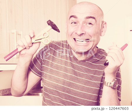 imposing man in prime of life holds in teeth of screws and holding hammer 120447603