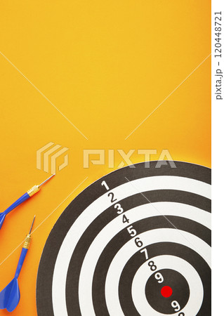 Dart board with blue darts on yellow background. Vertical photo. 120448721