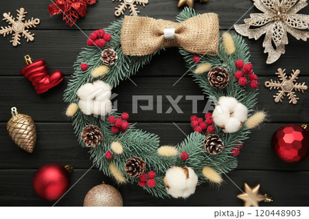 Wreath from fir, pine and spruce twigs, decorated with cotton, flowers ad christmas decoration on black wooden background Wreath from fir, pine and spruce twigs, decorated with cotton, flowers ad christmas decoration on black wooden background 120448903