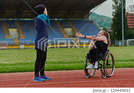 Two strong and inspiring women, one a Muslim wearing a burka and the other in a wheelchair stretching and preparing their bodies for a marathon race on the track 120449851