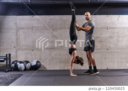 A muscular man assisting a fit woman in a modern gym as they engage in various body exercises and muscle stretches, showcasing their dedication to fitness and benefiting from teamwork and support A muscular man assisting a fit woman in a modern gym as they engage in various body exercises and muscle stretches, showcasing their dedication to fitness and benefiting from teamwork and support 120450025