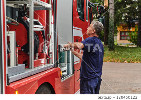 A dedicated firefighter preparing a modern firetruck for deployment to hazardous fire-stricken areas, demonstrating readiness and commitment to emergency response 120450122