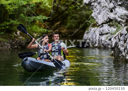A young couple enjoying an idyllic kayak ride in the middle of a beautiful river surrounded by forest greenery 120450130