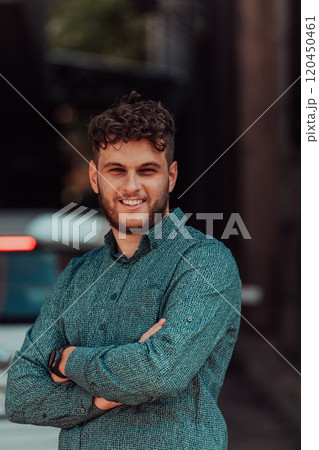 A successful young businessman in a shirt, with crossed arms, poses outdoors, confident expression on his face. 120450461