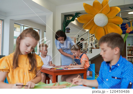 Creative kids during an art class in a daycare center or elementary school classroom drawing with female teacher. 120450486