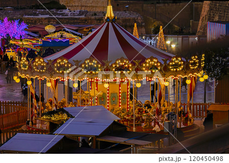 Brightly lit vintage carousel with a red and white striped canopy surrounded by glowing lights and festive decorations at night 120450498