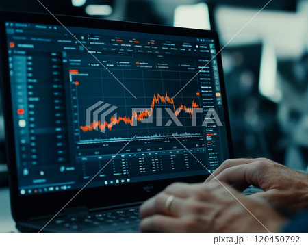 Close-up of hands typing on a laptop displaying financial graphs and data 120450792