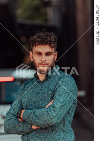 A successful young businessman in a shirt, with crossed arms, poses outdoors, confident expression on his face. 120450937