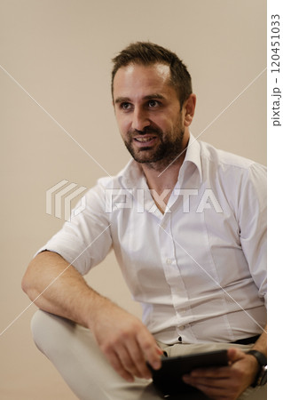 A confident businessman sitting and using laptop with a determined expression, while a beige background enhances the professional atmosphere, showcasing his productivity and expertise. A confident businessman sitting and using laptop with a determined expression, while a beige background enhances the professional atmosphere, showcasing his productivity and expertise. 120451033