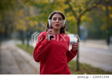 Young beautiful woman running in autumn park and listening to music with headphones on smartphone Young beautiful woman running in autumn park and listening to music with headphones on smartphone 120451340