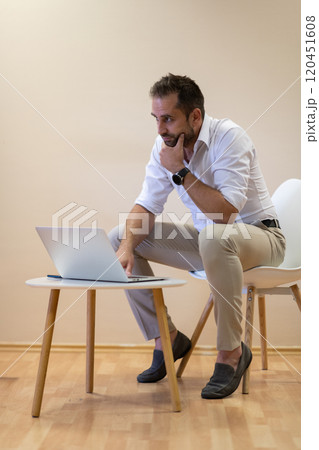 A confident businessman sitting and using laptop with a determined expression, while a beige background enhances the professional atmosphere, showcasing his productivity and expertise. A confident businessman sitting and using laptop with a determined expression, while a beige background enhances the professional atmosphere, showcasing his productivity and expertise. 120451608