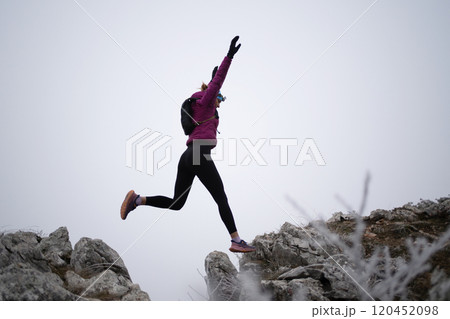 silhouette of a fitness woman trail runner jumping over a cliff and running to a rocky mountain top silhouette of a fitness woman trail runner jumping over a cliff and running to a rocky mountain top 120452098