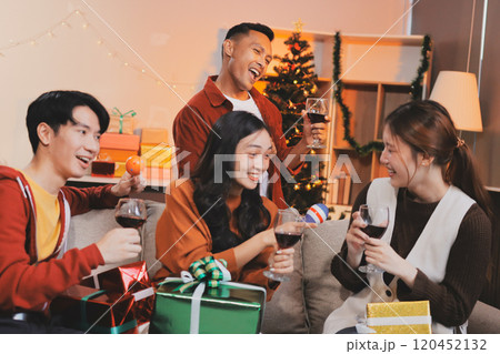 Group of young Asian man and women as friends having fun at a New Year's celebration, holding gift boxes standing by Christmas tree decoration, midnight countdown Party at home with holiday season. 120452132