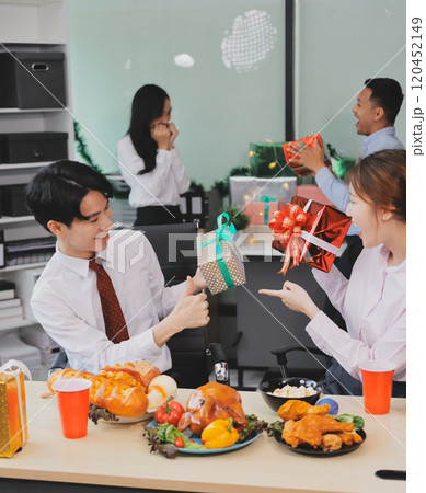 full length view of a group of business team wearing red Santa hat and exchange gift box together in the office for Christmas. 120452149