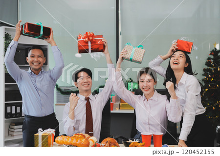 full length view of a group of business team wearing red Santa hat and exchange gift box together in the office for Christmas. 120452155