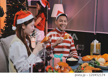Group of happy Asian friends celebrating Christmas and decorate the Christmas tree indoors. Beauty woman with Christmas Gifts. New Year party. Woman hands decorate Christmas tree red ball, bauble. 120452174