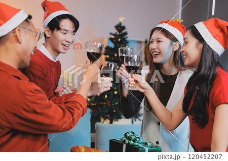 Group of young Asian man and women as friends having fun at a New Year's celebration, holding gift boxes standing by Christmas tree decoration, midnight countdown Party at home with holiday season. 120452207