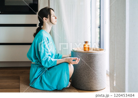 Young woman practicing self-care with aromatherapy and candles in a peaceful indoor setting. Relaxation and mindfulness concept. Young woman practicing self-care with aromatherapy and candles in a peaceful indoor setting. Relaxation and mindfulness concept. 120453484