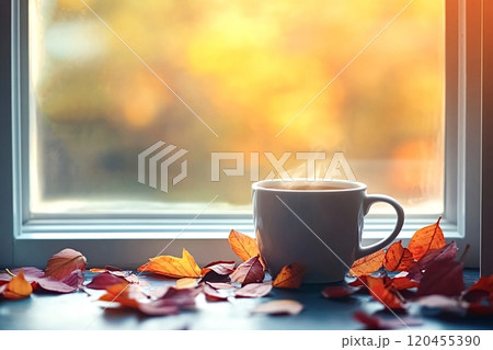 Steaming cup of coffee resting on window ledge with autumn leaves 120455390