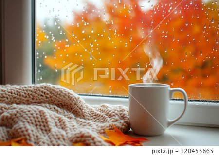 A cozy autumn scene with an open window, showcasing colorful leaves and falling raindrops outside, while inside there's steam rising from the coffee mug on the windowsill. A cozy autumn scene with an open window, showcasing colorful leaves and falling raindrops outside, while inside there's steam rising from the coffee mug on the windowsill. 120455665