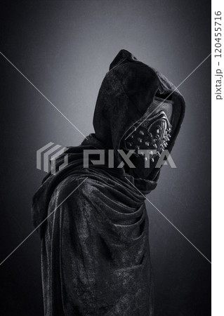 Scary figure in hooded cloak with spike studs mask at night over dark misty background 120455716