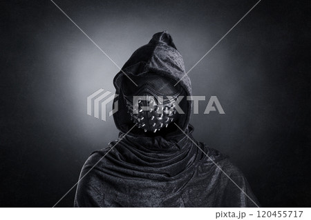Scary figure in hooded cloak with spike studs mask at night over dark misty background 120455717