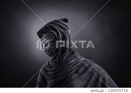 Scary figure in hooded cloak with spike studs mask at night over dark misty background 120455718