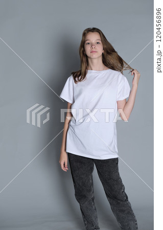 A teenage girl stands in a white t-shirt, gazing to the side with a pensive look. This portrait emphasizes the curiosity and inner reflections common during teenage years. 120456896