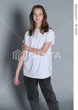A teenage girl stands in a white t-shirt, gazing to the side with a pensive look. This portrait emphasizes the curiosity and inner reflections common during teenage years. 120456905