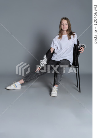 The young girl sits comfortably on a chair, her relaxed pose exuding quiet confidence. This image highlights the simplicity and authenticity of youthful moments in contemporary lifestyle. 120456943