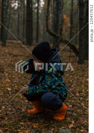 A child lost in the forest wipes his face from tears with his hand. A lost child cries and squats in the forest wearing orange boots feeling scared and alone in this wilderness. A child lost in the forest wipes his face from tears with his hand. A lost child cries and squats in the forest wearing orange boots feeling scared and alone in this wilderness. 120457612