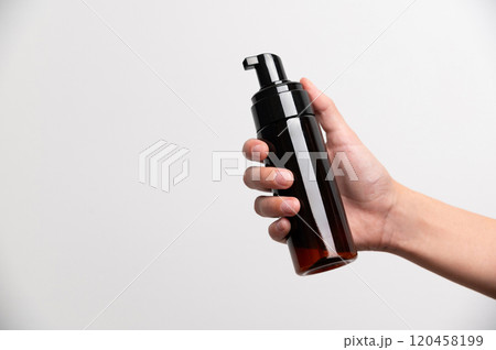 Hand of young caucasian woman holding dark brown tube with dispenser on white background Hand of young caucasian woman holding dark brown tube with dispenser on white background 120458199