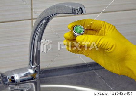 person in yellow rubber gloves changing clogged faucet aerator 120459404
