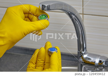 replacing a clogged faucet aerator with a new one. plumber in yellow rubber gloves holding an aerator replacing a clogged faucet aerator with a new one. plumber in yellow rubber gloves holding an aerator 120459412